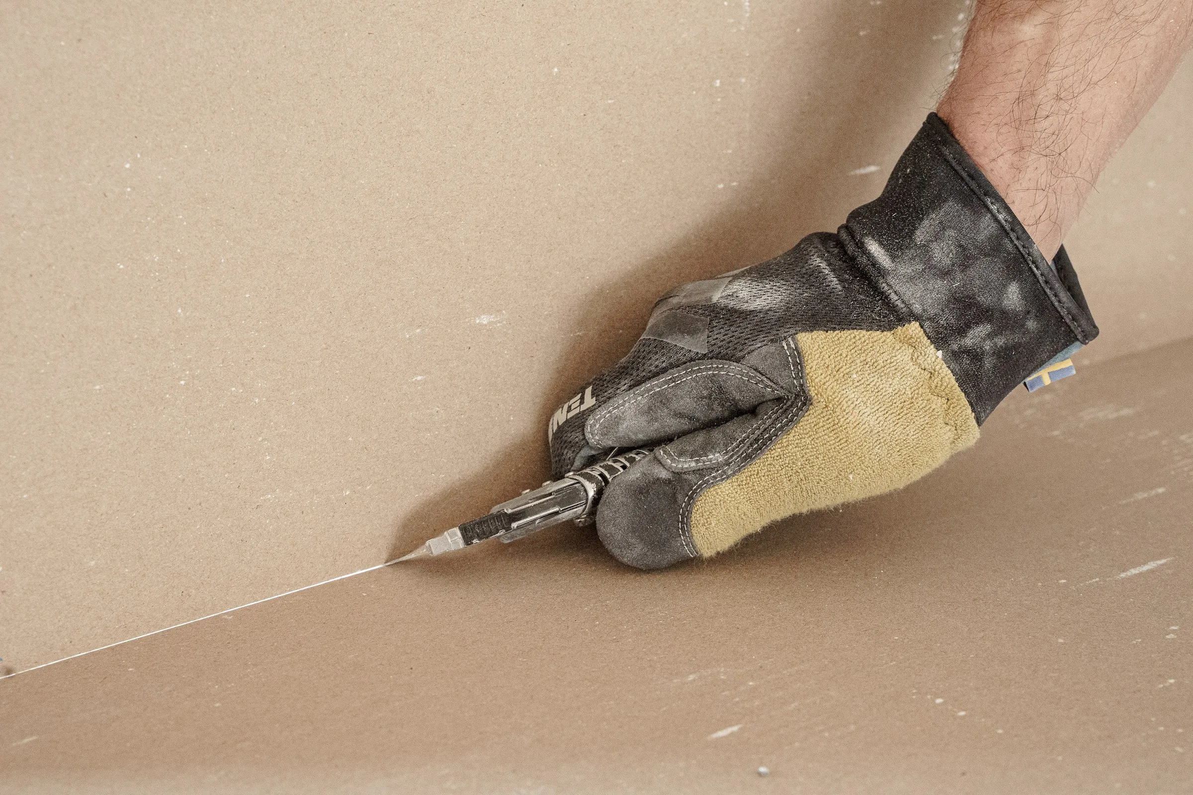 Hand im Arbeitshandschuh beim Zuschneiden einer Gipskartonplatte